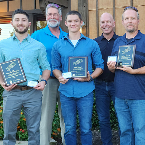 Group of five male GE Vernova employees, three of which are newly certified apprentices holding their certification credentials and a plaque